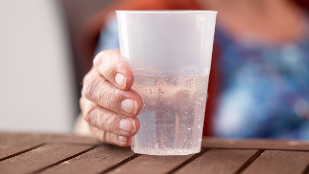 Die Hand einer alten Dame hält einen Plastikbecher mit Mineralwasser, Pflegeheim