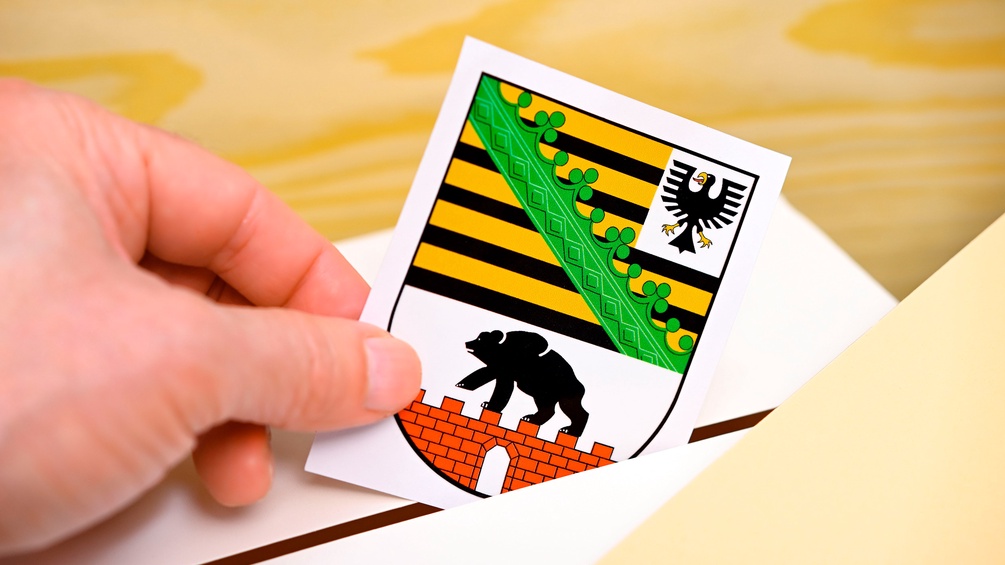 Hand wirft Landeswappen des deutschen Bundeslandes Sachsen-Anhalt in eine Wahlbox