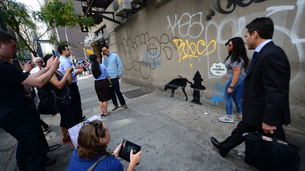 New York, 2013: Menschen fotografieren ein Grafitti von Banksy