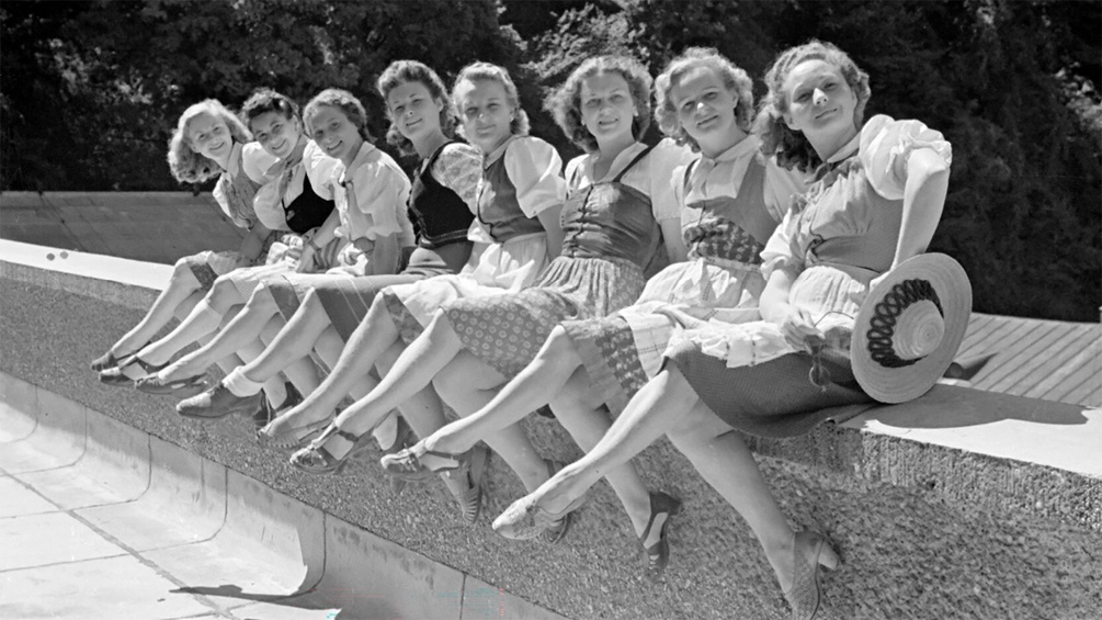 Frauen sitzen aufgereiht auf einer Steinmauer und posieren bei den Salzburger Festspielen 1946