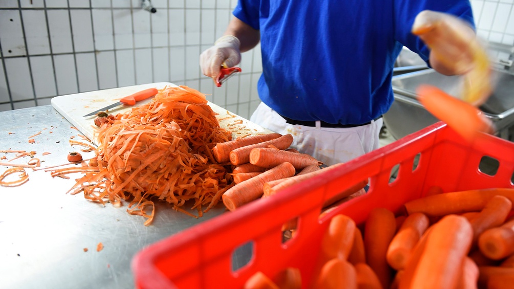 Mann schält eine große Menge Karotten