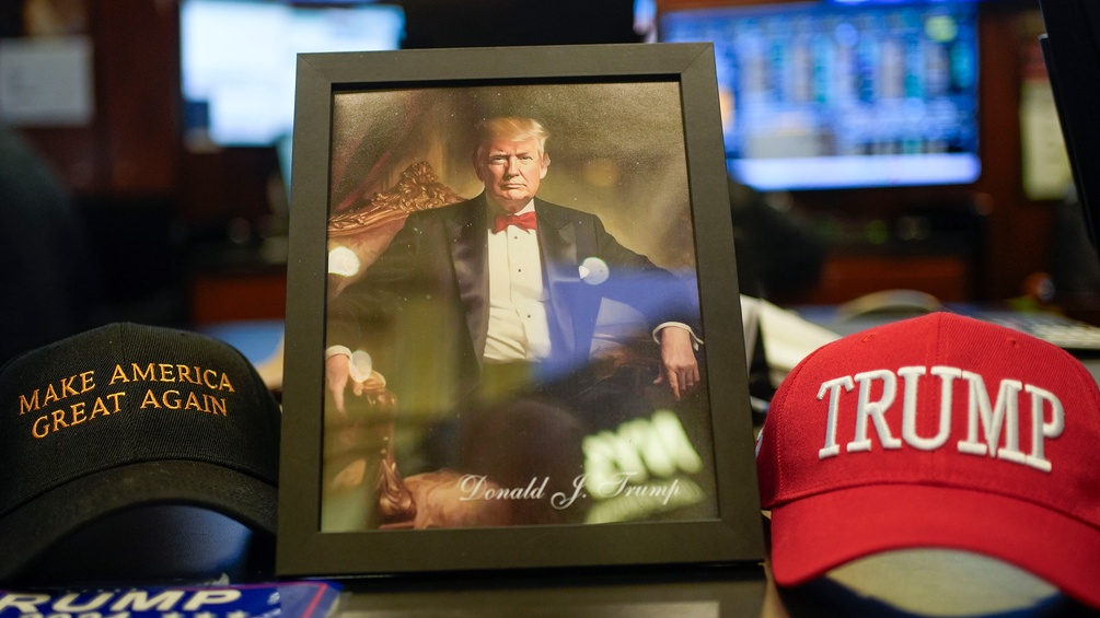 Foto von Donald Trump in einem Bilderrahmen neben MAGA-Kappen