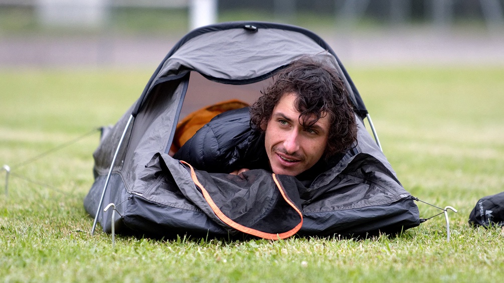 Ein Mann liegt in einem sehr kleinen Zelt.