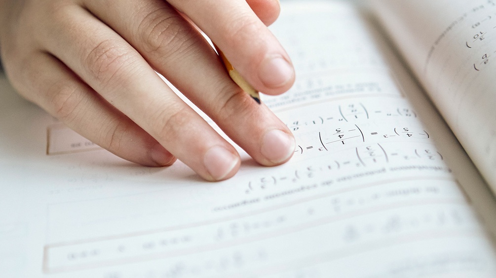 Hand mit Bleistift und Mathematikbuch