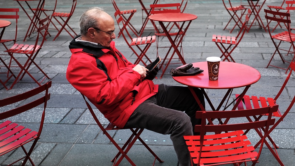 Ein Mann sitzt alleine in einem Gastgarten mit einem Handy in der Hand