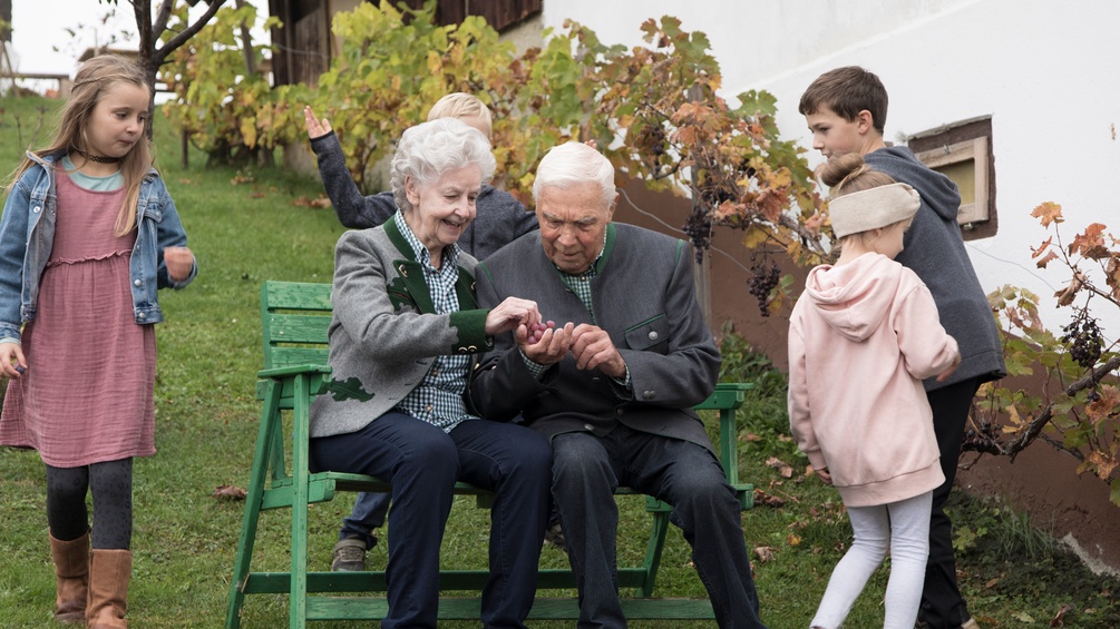 ULLA SLADE Zwei ältere Menschen mit Kindern am Hof