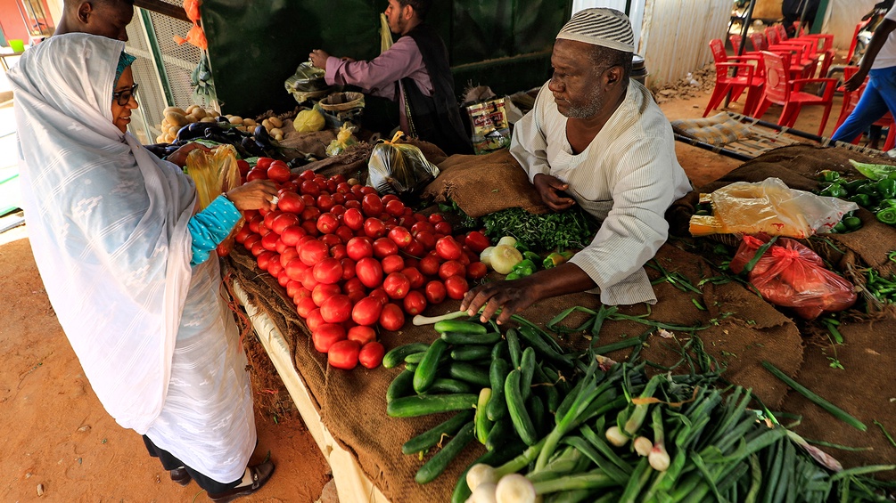 Eine Frau kauft Gemüse von einem Markstand im Sudan.