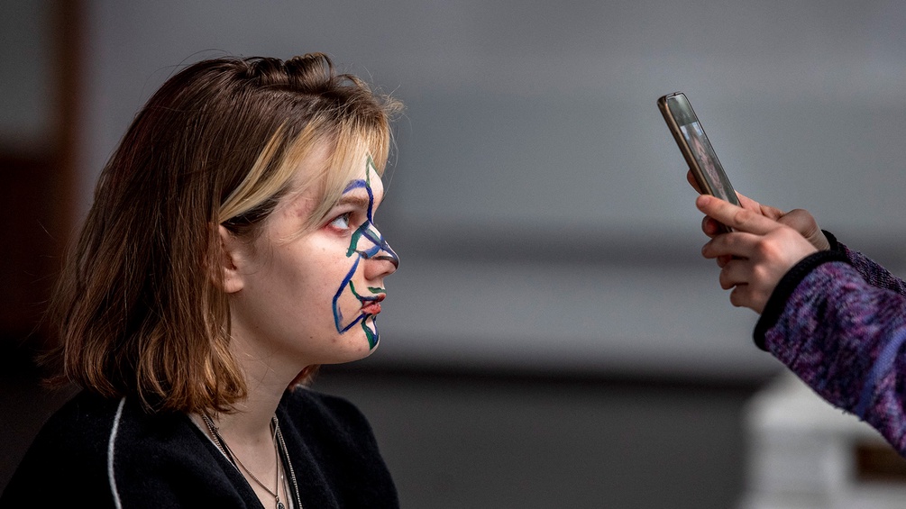 Frau mit Bemalung im Gesicht, Handy - Protest gegen Gesichtserkennung.