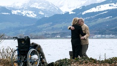 Mann und Frau umarmen sich an einem See, Rollstuhl