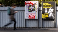 Eine Person geht an Plakaten der Kampagne „Nein zur Halbierung des SRG SSR“ vorbei. Die Slogans lauten: "Zerstörung des Zusammenhalts" und "Gegen die Volksinitiative 200 Franken sind genug"