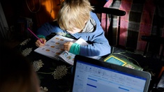 Ein Kind lernt am Tisch mit der Mutter welche am Laptop im Homeoffice arbeitet.