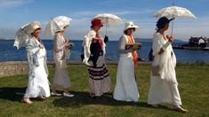Fünf verkleidete Damen mit Büchern und Sonnenschirmen