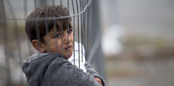 Flüchtlingskind an einem Bauzaun
