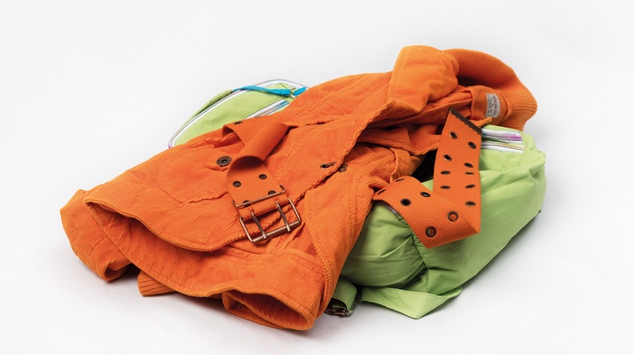 Jacke mit Gürtel liegt auf einer hellgrünen Tasche