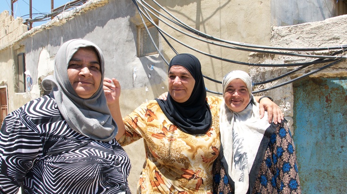 Drei libanesische Frauen stehen vor ihrem Haus in der Armensiedlung und lächeln in die Kamera.