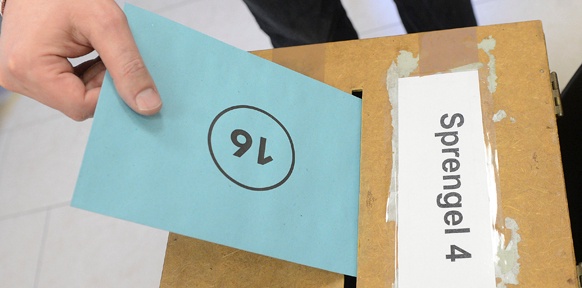 Stimmzettel wird in die Wahlurne geworfen