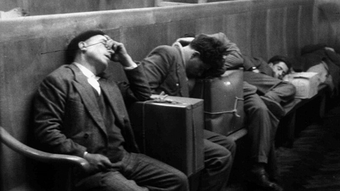 Männer schlafen in einer Wartehalle auf ihre Koffer gestützt