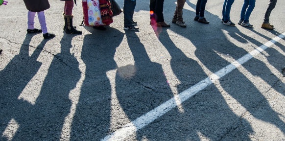Flüchtlinge stehen in einer Reihe und werfen Schatten auf den Boden