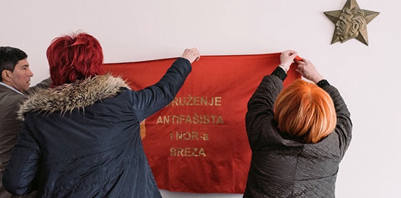 Zwei Frauen und ein Mann hängen eine Rote Fahne auf