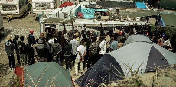 Flüchtlinge in Calais stehen vor einem Zelt.