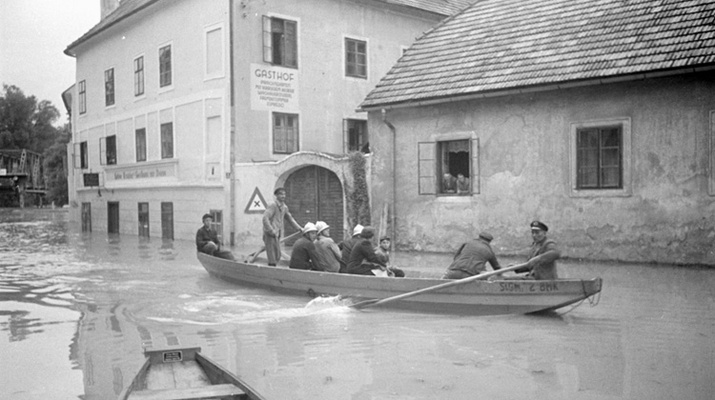 Hochwasserschäden in Linz und Umgebung 1954: Feuerwehrmänner fahren in Zille durch eine überschwemmte Straße.