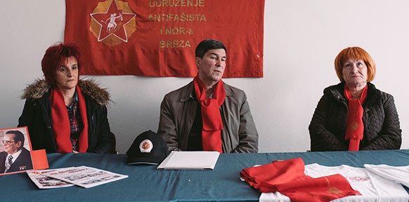 Zwei Frauen und ein Mann sitzen vor der roten Fahne.