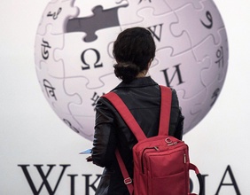 Frau mit Rucksack steht vor Wikipedia-Plakat