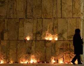 Eine Frau geht an Kerzenlichtern an einer Wand vorbei.