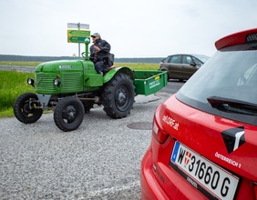 Mann auf Traktor und Ö1 Auto