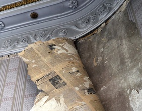 Tapete löst sich von einer Wand und alte Zeitungen tauchen darunter auf.