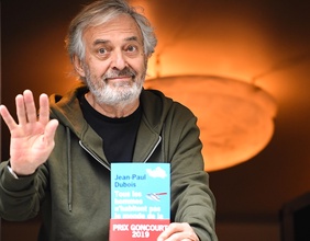 Jean-Paul Dubois posiert mit seinem Buch an einem  Fester 