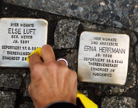 Eine Frau putzt Erinnerungssteine von deportierten jüdischen Opfern