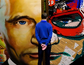 Ein junger Mann steht vor einem Gemälde von Putin.