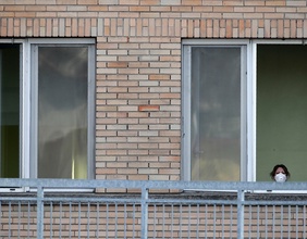 Frau mit Mundschutz schaut aus dem Fenster