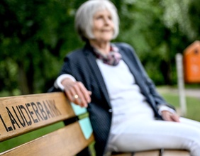 Eine ältere Frau sitzt auf der Plauderbank.