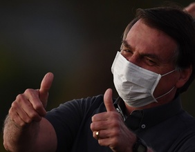 Bolsonaro hält die Daumen in die Höhe währrend er eine Maske trägt.