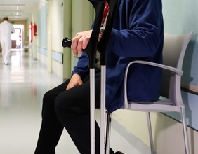 Mann nach einer Hüft-OP auf einer Bank sitzend mit Krücken, Krankenhaus