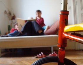 Dreirad, dahinter Menschen auf einem Sofa lesend