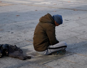 Ein Obdachloser sitzt mit gebeugtem Haupt auf der Strasse