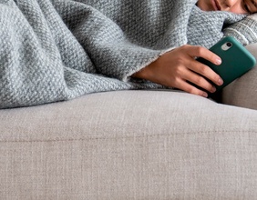 Doom scrolling, Frau mit Smartphone auf einer Couch liegened