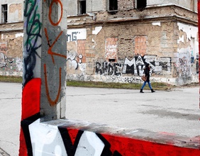 Alltagsaufnahme in Sarajevo, Frau geht an einer Ruine vorbei Graffiti