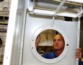 Ein Mechaniker schaut durch die Trommelöffnung eines Waschmaschinengehäuses.
