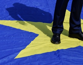 Ein Mann im Anzug steht auf dem Stern einer EU Flagge.