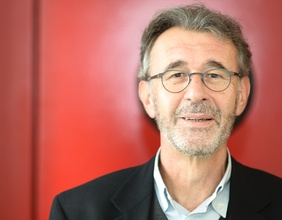 Porträt von Peter Klein vor rotem Hintergrund.