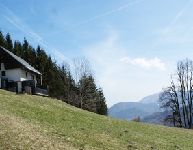 Das Haus der Alma Zsolnay am Semmering auf einer grünen Wiese. Dahinter Berge und blauer Himmel.