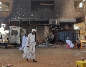 Menschen im Sudan vor einem vebrannten Haus.