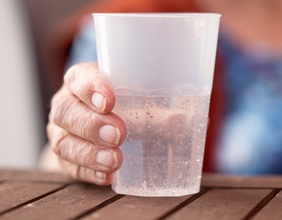 Die Hand einer alten Dame hält einen Plastikbecher mit Mineralwasser, Pflegeheim