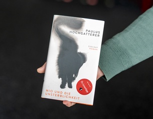 Das Buch "Mio und die Unsterblichkeit" wird in die Kamera von einer Männerhand gehalten