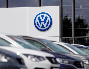 Großes VW-Zeichen bei einem Autohändler, diverse Autos im Vordergrund in Unschärfe