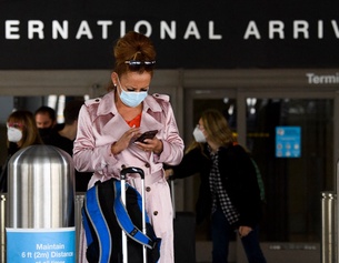 AFP/PATRICK T. FALLON Eine Frau am Flughafen mit Maske und Gepäck.